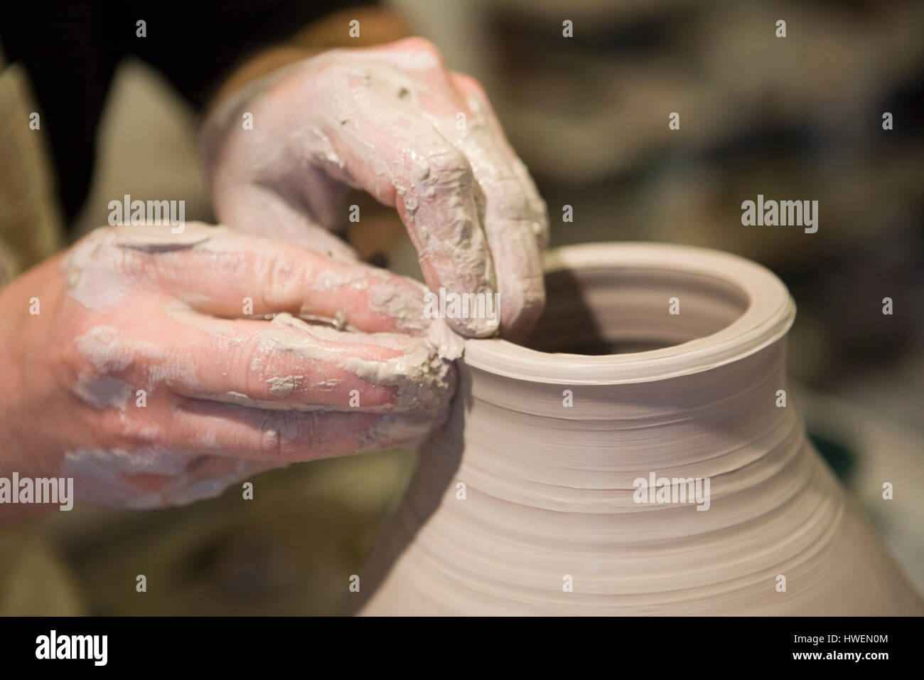 Close up potter maschio con le mani in mano la sagomatura pentola di creta sulla ruota di ceramiche in officina Foto Stock