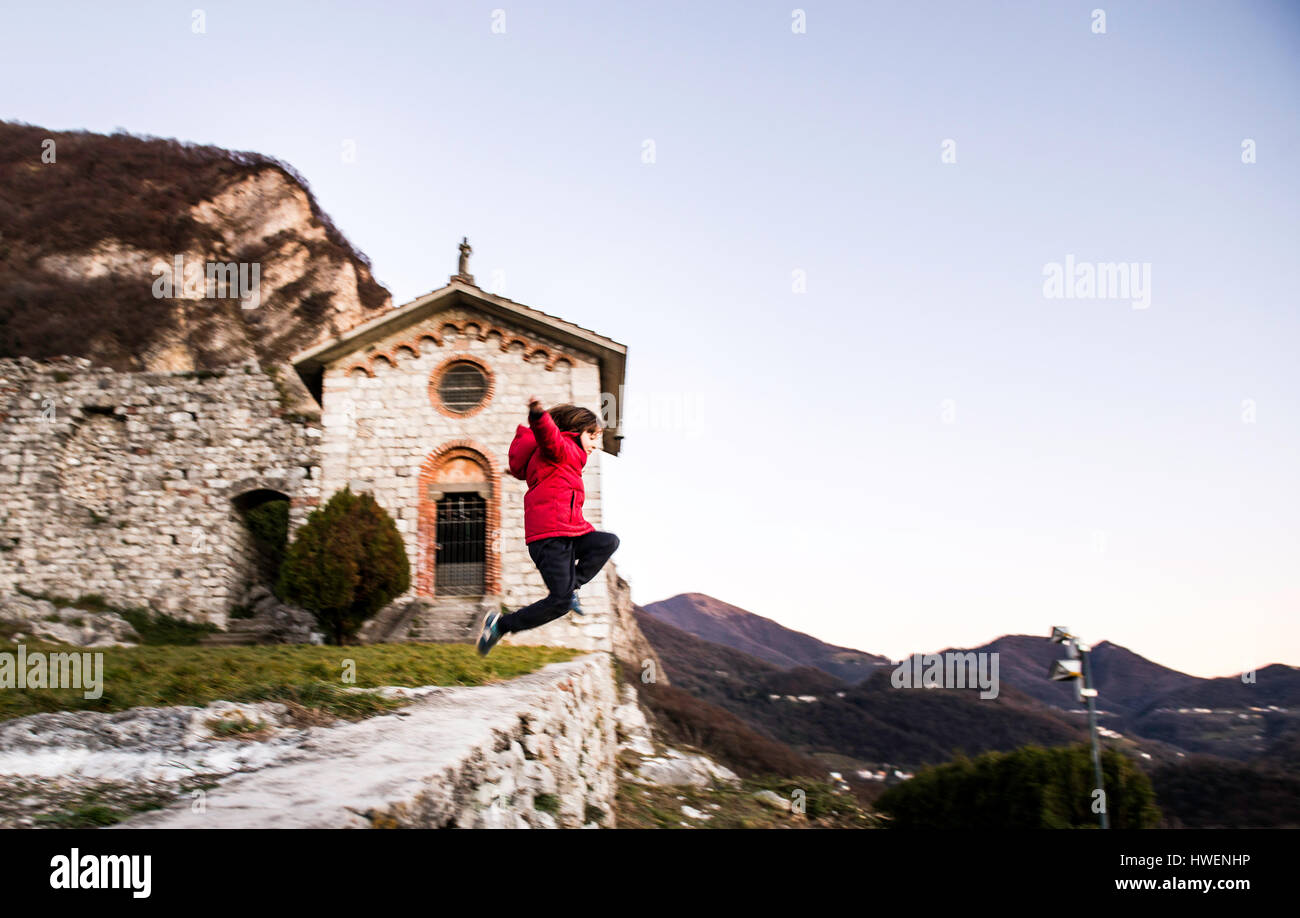 Ragazzo saltare da un alto muro nel paesaggio di montagna, Italia Foto Stock