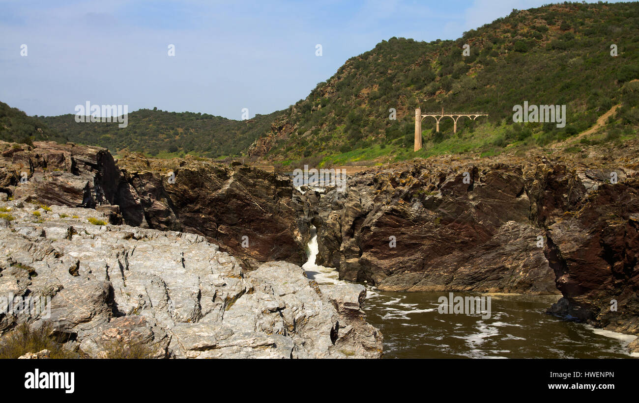 Panorama del Pulo do Lubo cascata al fiume Guadiana valley natural park. Fortemente eroso roccia scistosa. Offuscato il cielo blu e una di acqua torre di misurazione Foto Stock