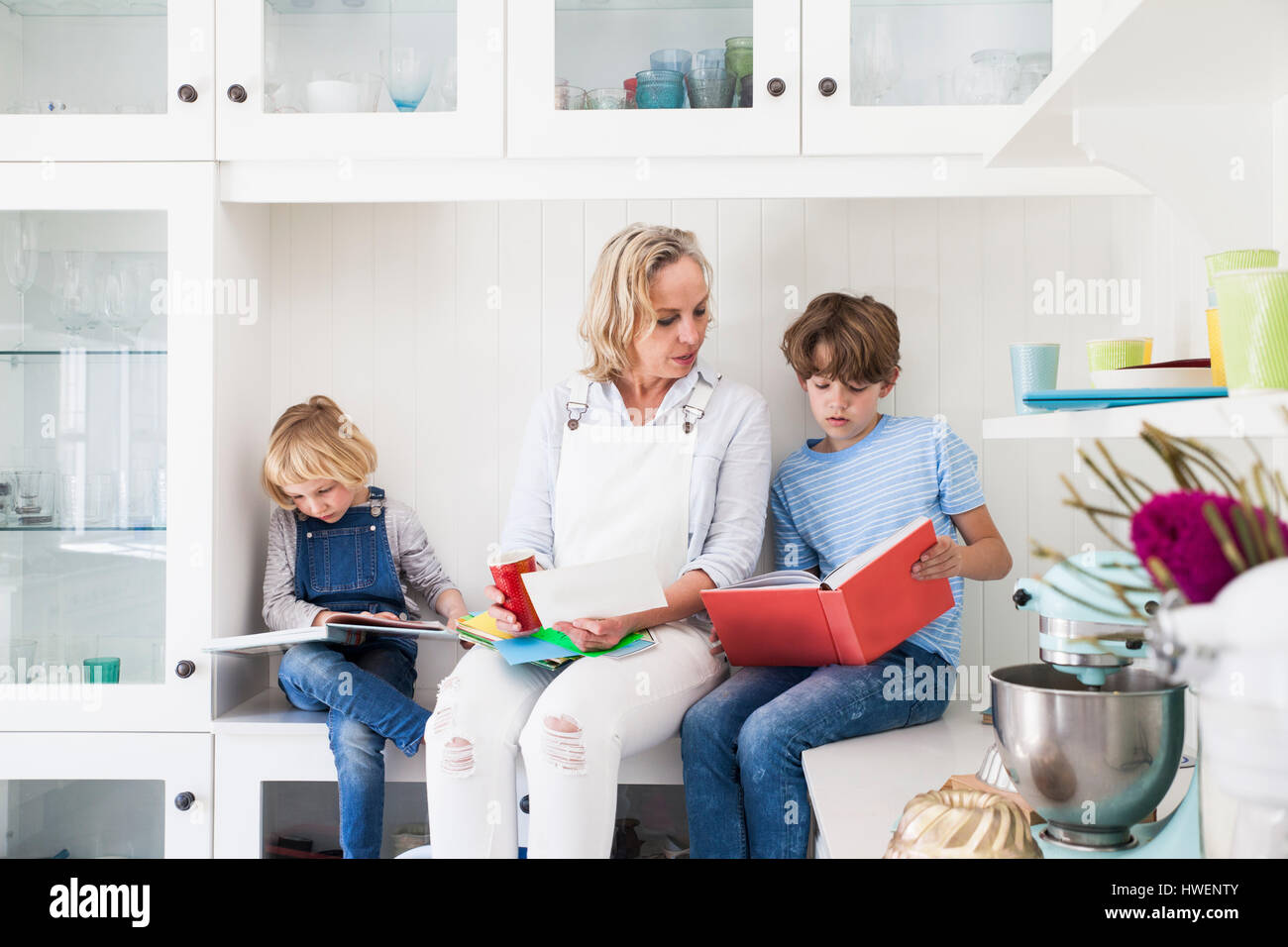 Donna matura seduta sul banco di cucina la lettura di libri illustrati con il figlio e la figlia Foto Stock