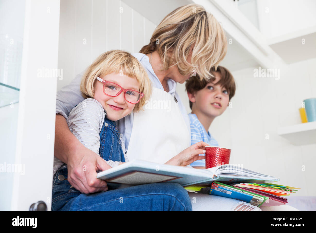 Donna matura seduta sul banco di cucina la lettura di libri illustrati con il figlio e la figlia Foto Stock