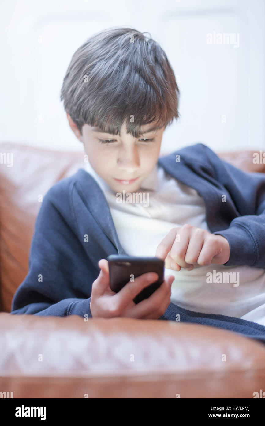 Ragazzo giocando con lo smartphone sul divano Foto Stock