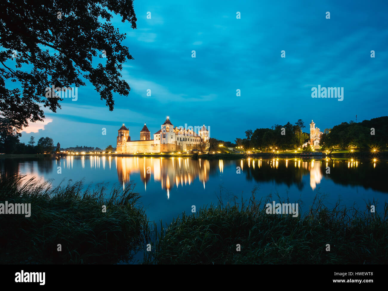 Mir, Bielorussia. Complesso del Castello di Mir In brillante illuminazione serale con candelette di riflessioni sul lago di acqua. Famoso punto di riferimento, antico monumento gotico del feudo Foto Stock