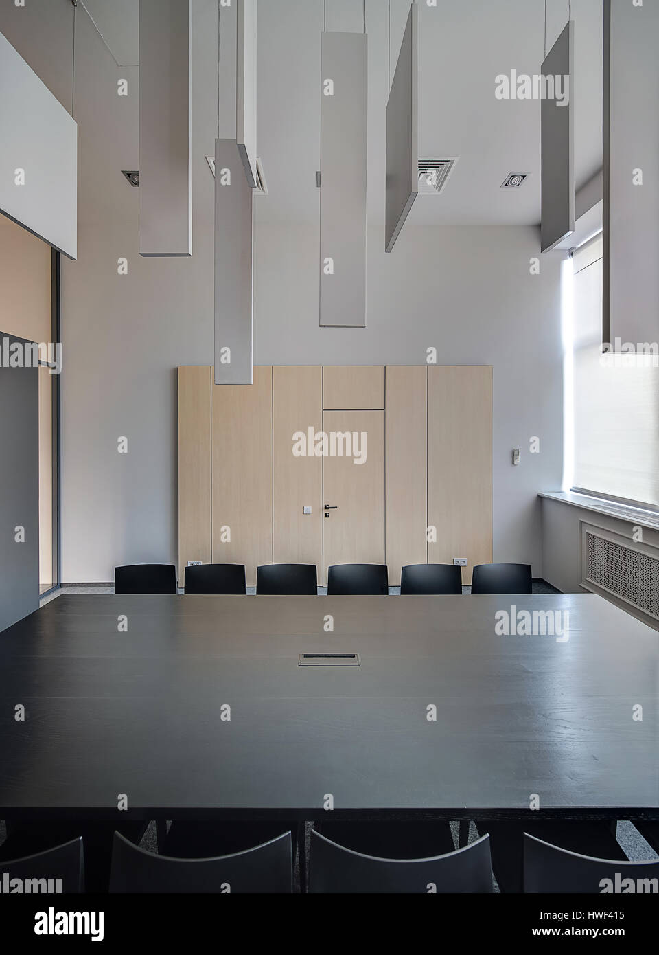 Grandi tavoli in legno nero con molte sedie in legno chiaro sfondo armadietti nella hall in stile loft con pareti di colore grigio. Ci sono parecchi hangin Foto Stock