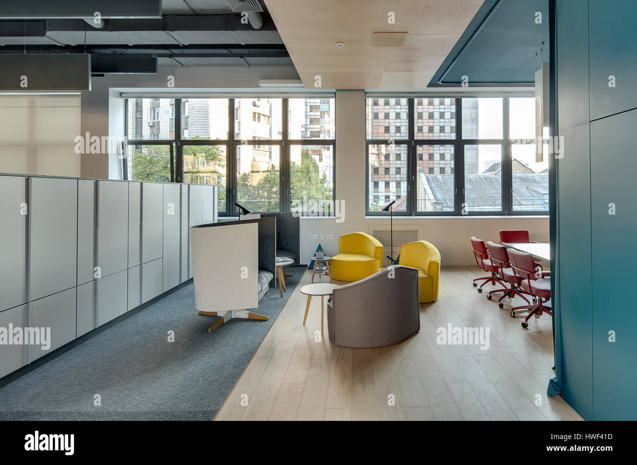 Coworking in stile loft con pareti chiare e grandi finestre. Vi è una zona relax con diverse poltrone morbido e rotondo piccolo tavoli in legno, tabella Foto Stock