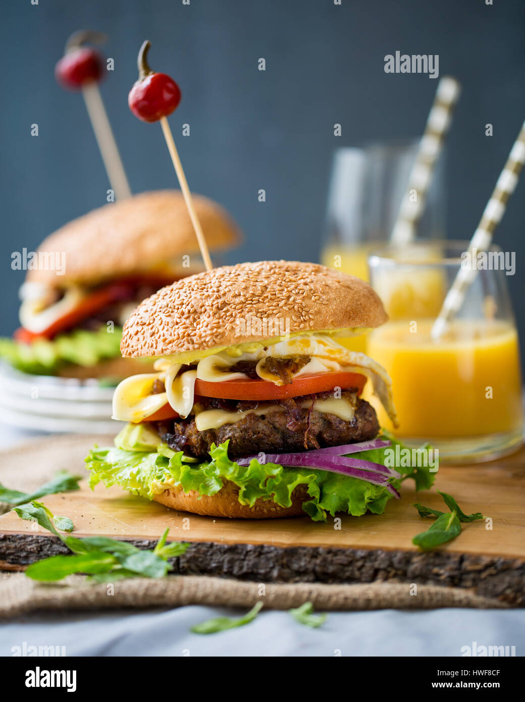 Due hamburger fatti in casa con verdure fresche, carne, cipolle caramellate e formaggio sulla tavola di legno Foto Stock