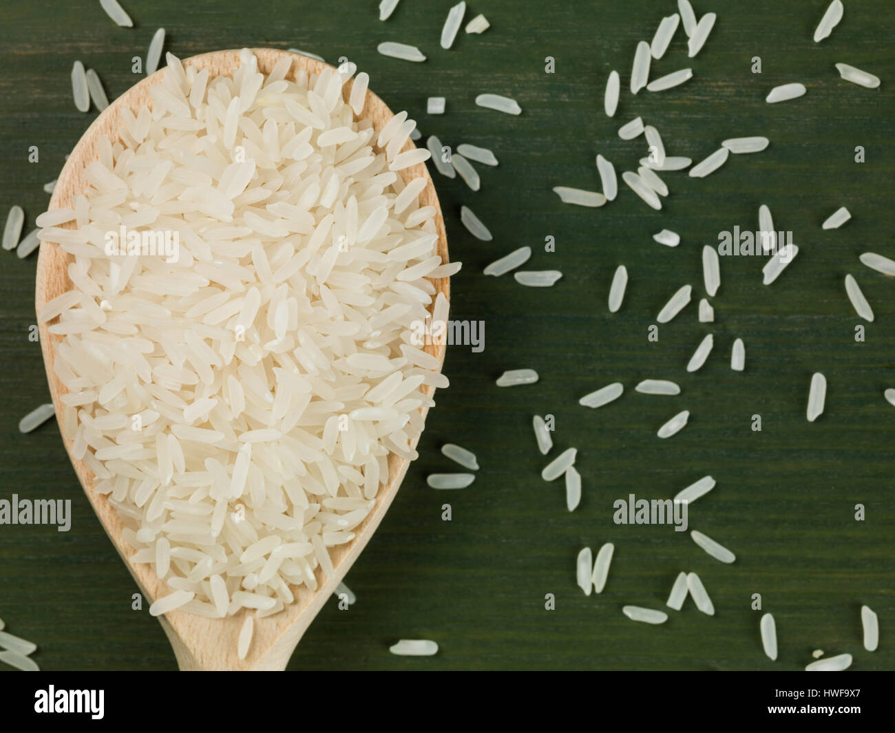 1 cucchiaio di legno essiccato del riso a grani lunghi contro uno sfondo verde Foto Stock