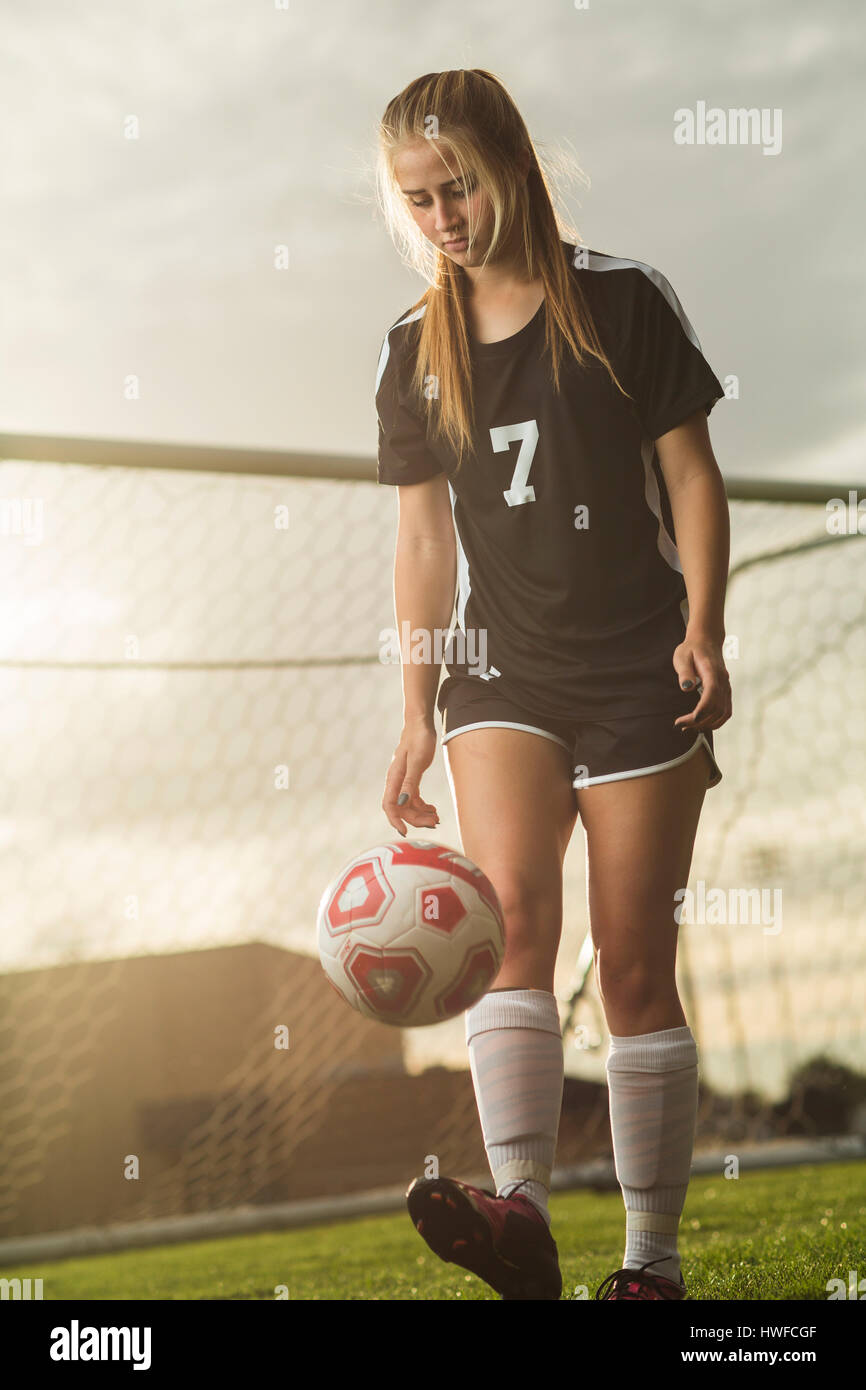 Basso angolo vista del giocatore di calcio calci palla sul campo sotto il cielo al tramonto Foto Stock