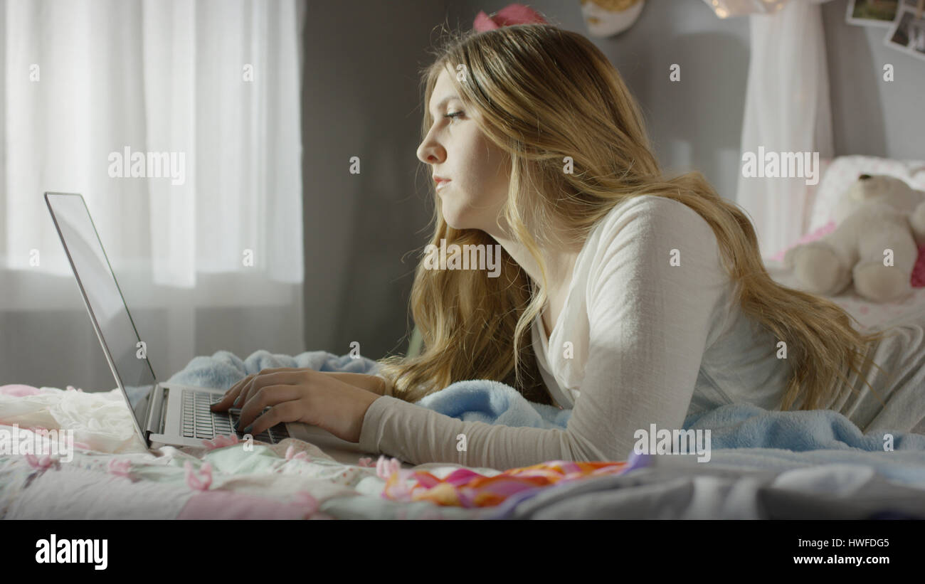 Profilo di grave ragazza adolescente utilizzando laptop a letto Foto Stock