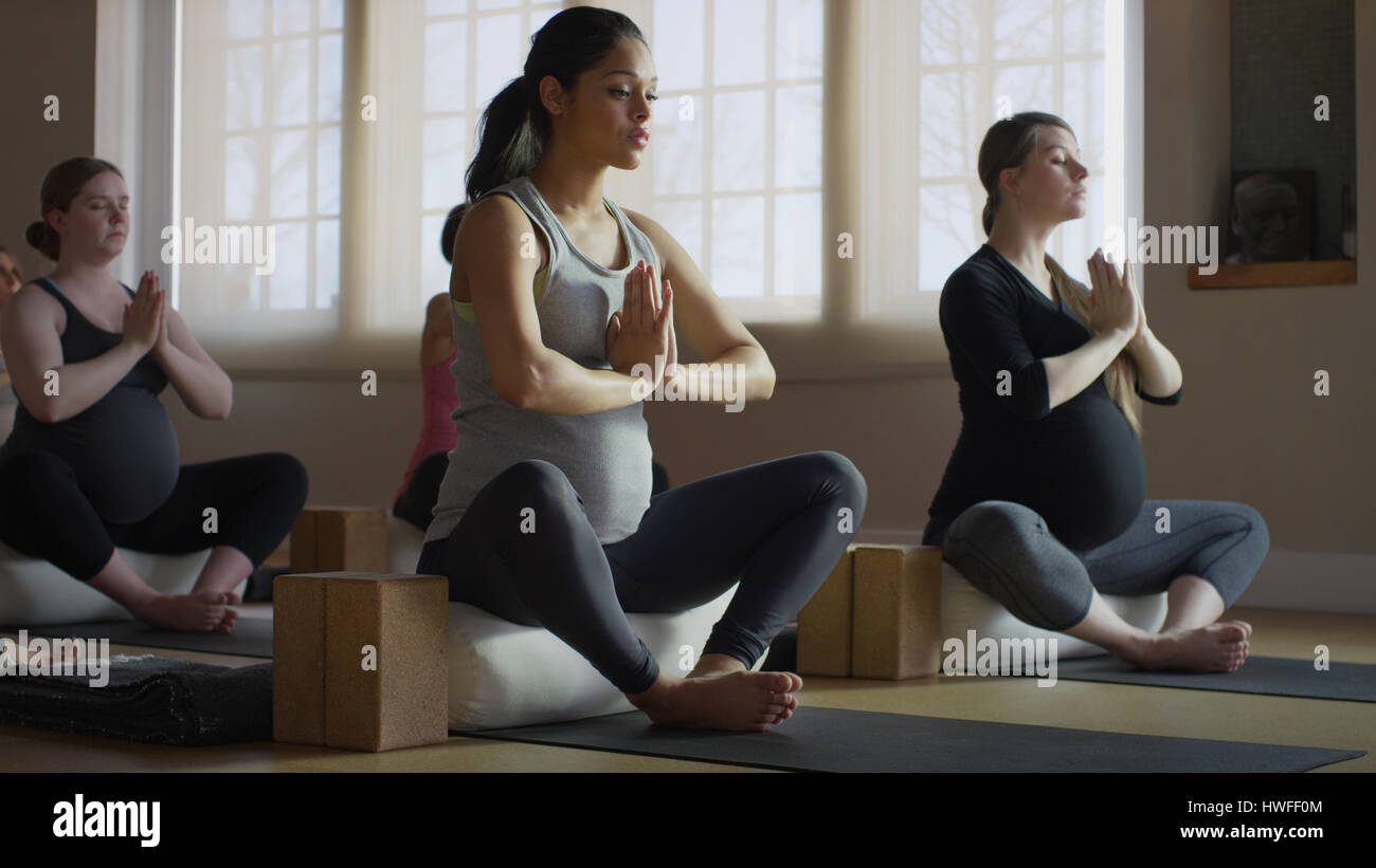 Donna incinta seduta con le gambe incrociate e la meditazione yoga in classe Foto Stock