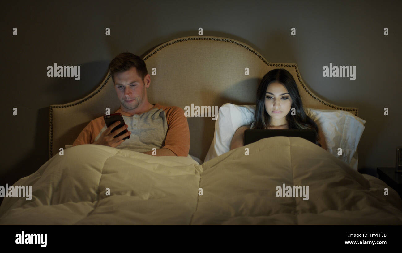 Distratti giovane utilizzando laptop e telefono cellulare separatamente in camera da letto Foto Stock