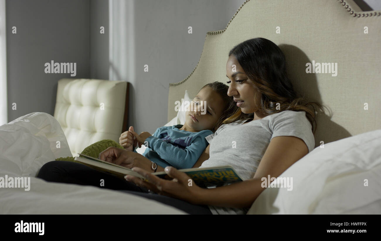 Rilassante la madre e il figlio la lettura di un libro sul letto Foto Stock