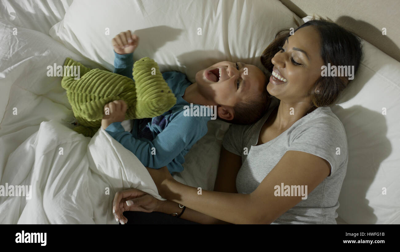Elevato angolo di visione madre solletico giocoso figlio nel letto Foto Stock
