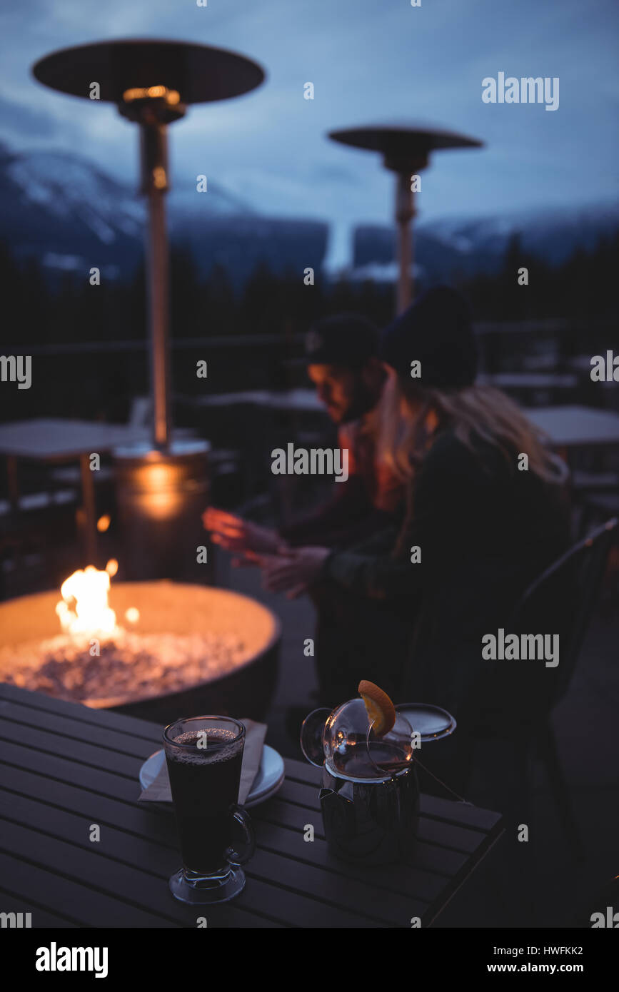 Giovane seduto da una buca per il fuoco al tramonto durante il periodo invernale Foto Stock