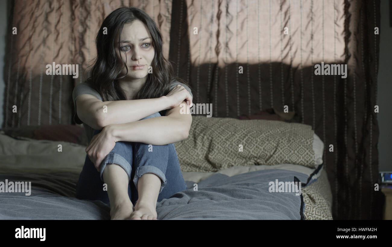 Triste martoriata donna tenendo le sue ginocchia e piangere sul letto Foto Stock