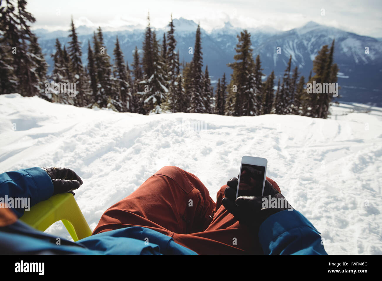 Sezione bassa dell'uomo tenendo il telefono cellulare al coperto di neve montagna contro alberi Foto Stock
