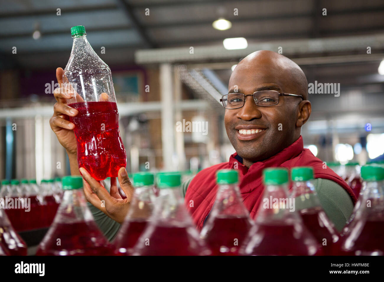 Ritratto di sorridere lavoratore di sesso maschile che mostra la bottiglia di succo in fabbrica Foto Stock