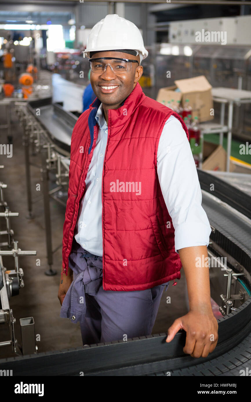 Ritratto di felice dipendente di sesso maschile in piedi dal nastro trasportatore in fabbrica Foto Stock