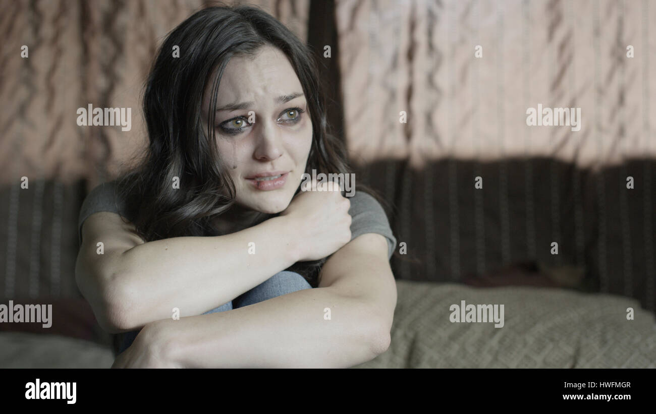 Triste martoriata donna tenendo le sue ginocchia e piangere sul letto Foto Stock