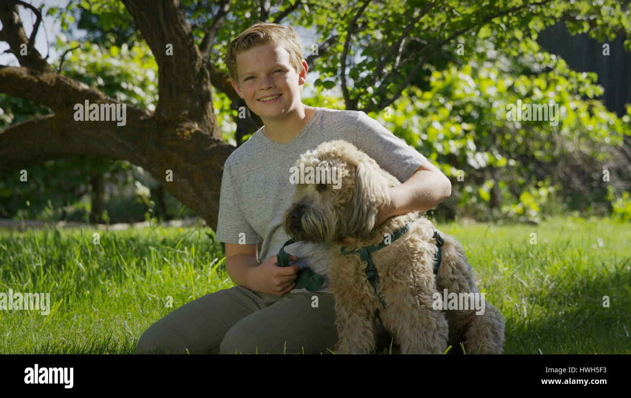 Angolo basso ritratto di sorridere ragazzo seduto con cane sul prato Foto Stock