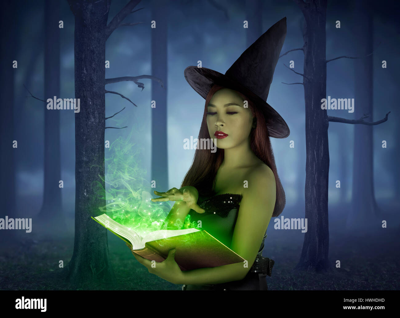 Bella ragazza asiatica indossando panno strega incantesimo di lettura nel libro sulla foresta di notte Foto Stock