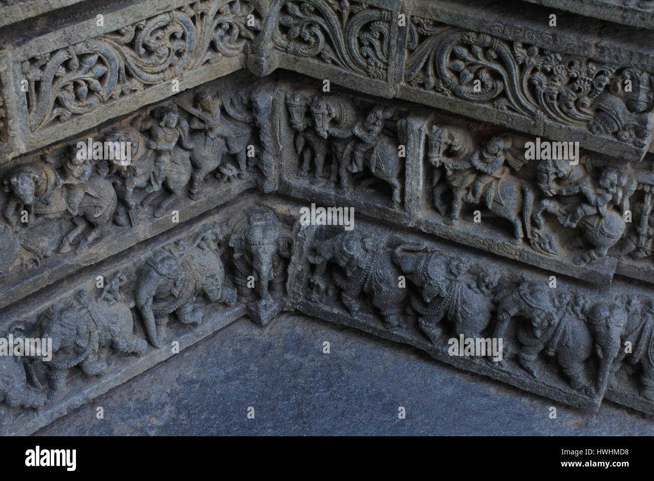 Close up di sculture in pietra di fogliame, guerrieri , cavalieri, elefante processione in cui due parete ad angolo di soddisfare ogni altro sulla parete del santuario a Chennakesa Foto Stock