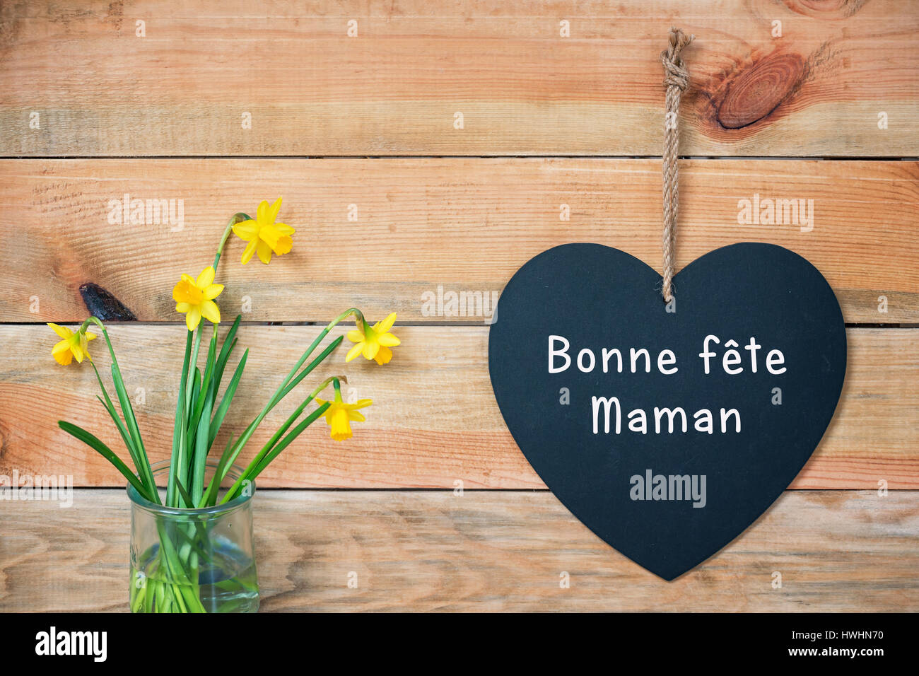 Bonne fete maman, mamme francesi giorno della carta, legno tavole con i narcisi e una lavagna a forma di cuore Foto Stock
