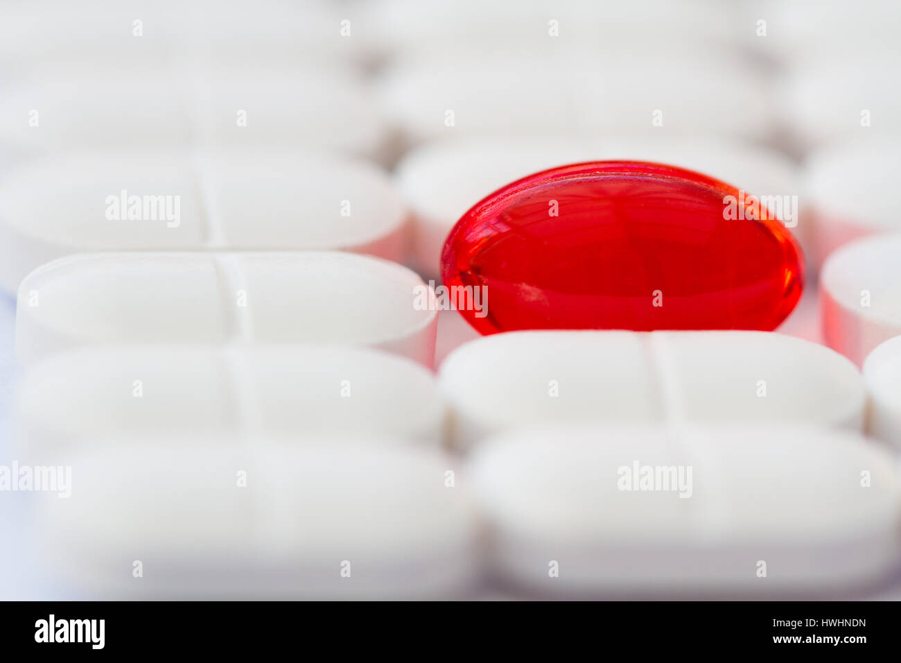 Una singola capsula rossa della medicina in piedi fuori contro le righe bianche di sollievo dal dolore compresse, pillole e farmaci in medicina di una immagine di sfondo. Foto Stock