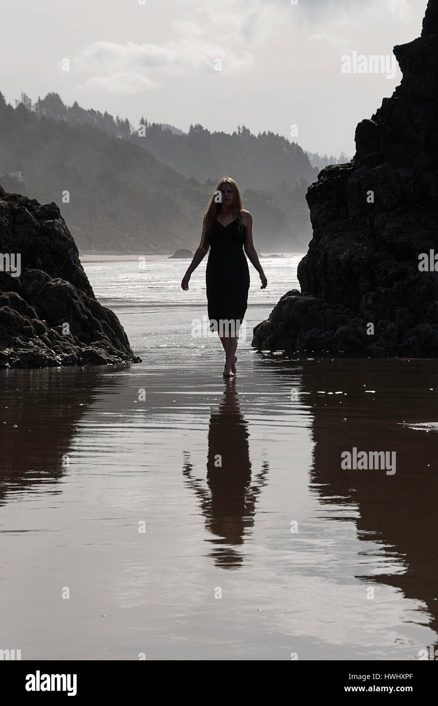 Una donna in piedi in acqua sulla costa dell'Oregon. Foto Stock