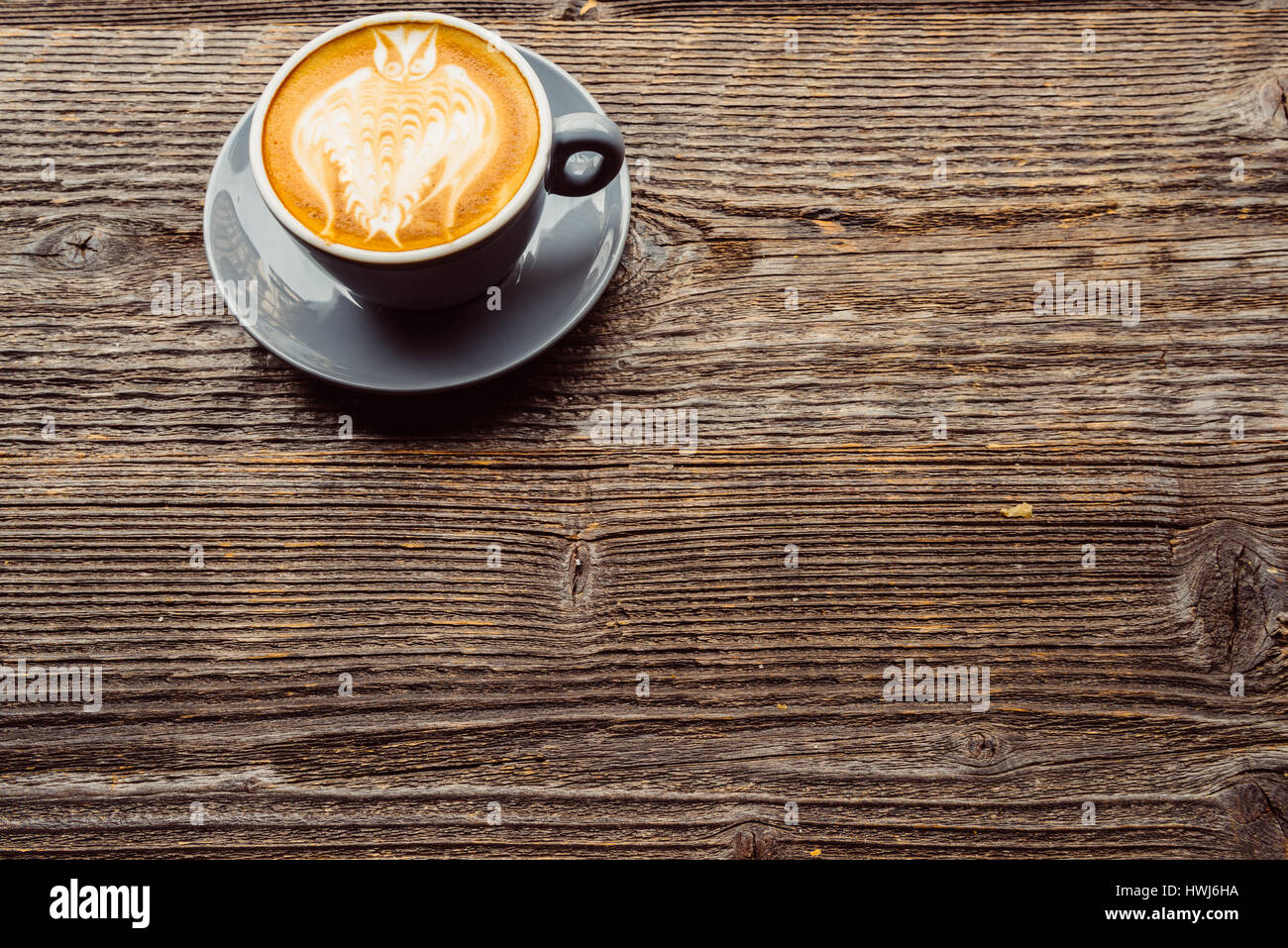 Cappuccino con schiuma di latte disegnata a forma di un gufo, isolata su una tavola di legno Foto Stock