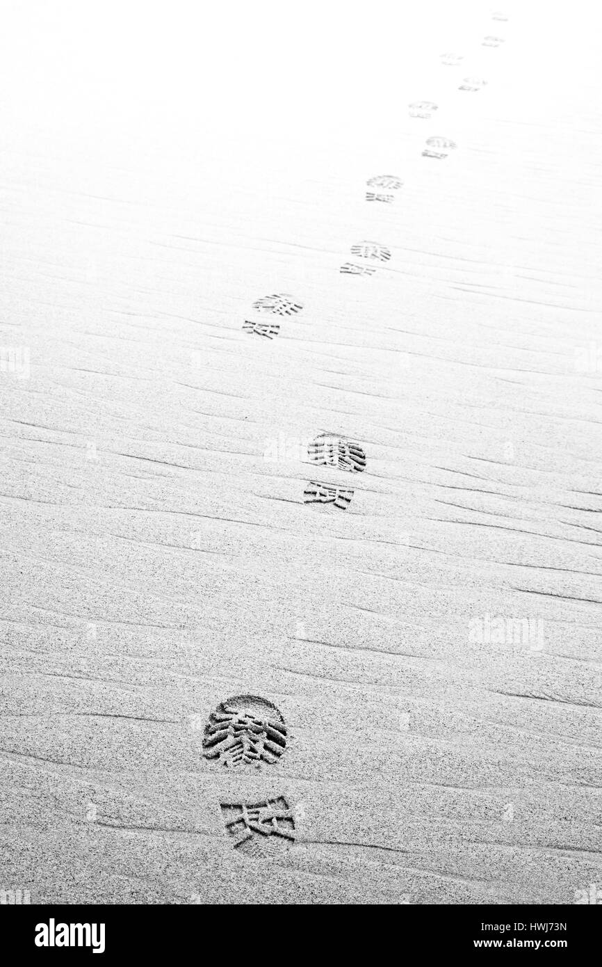 Footprints scarpe da trekking sulla spiaggia ,Dissolvenza al bianco. Monocromatico Foto Stock