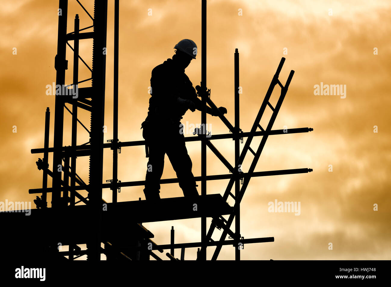 Silhouette di un lavoratore edile contro sky sul ponteggio con scaletta sul sito di costruzione al tramonto Foto Stock