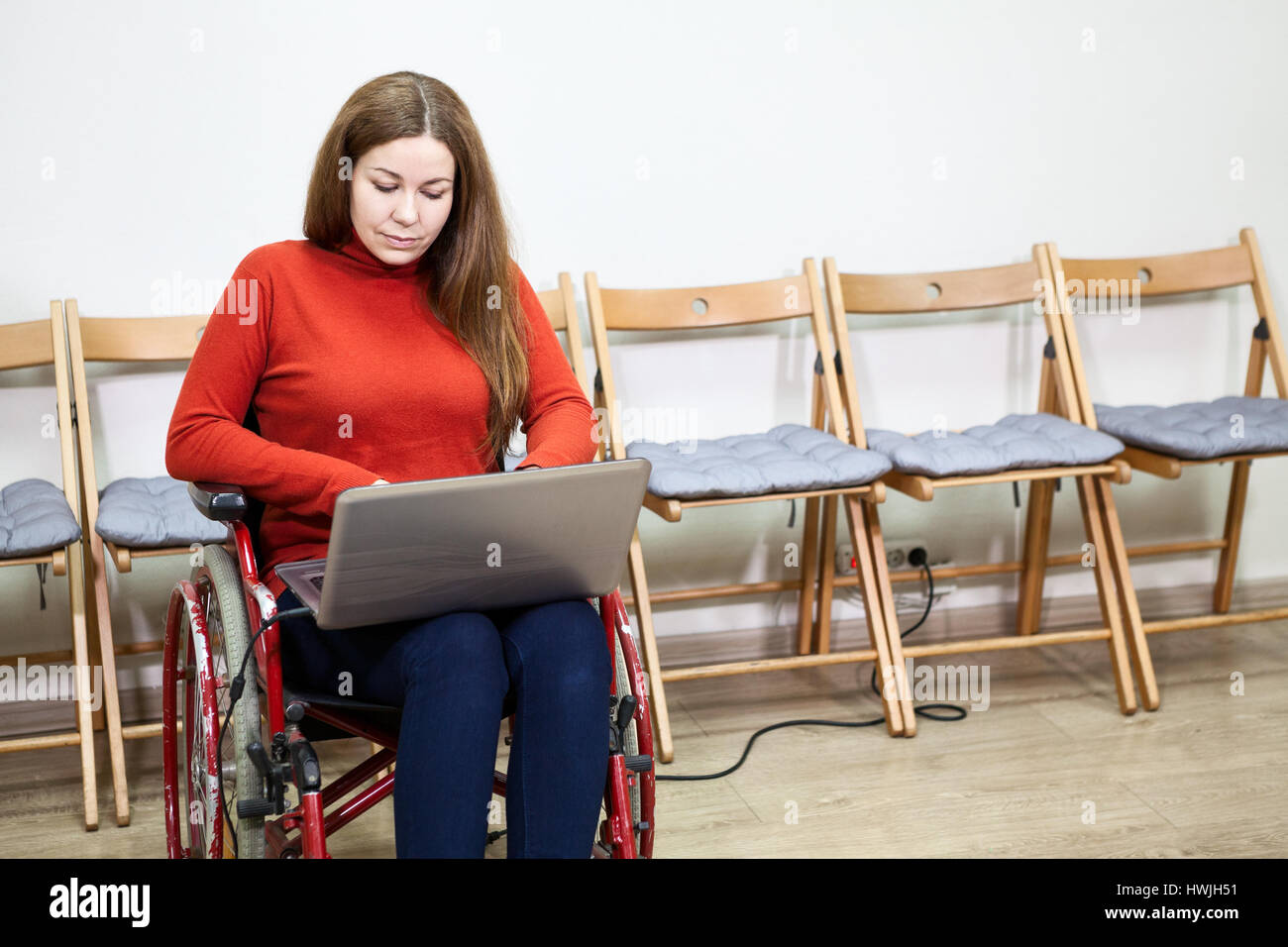 Bella disabili caucasica donna seduta in sedia a rotelle e di lavorare con il computer portatile indoor Foto Stock