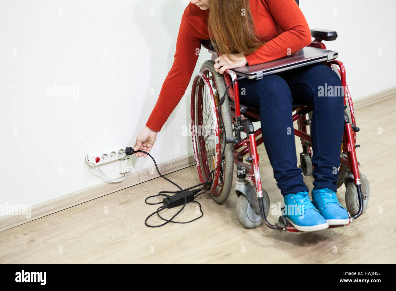 Disabili donna caucasica presenta alcuni problemi durante l'inserimento della spina di alimentazione. Sedia a rotelle seduta Foto Stock