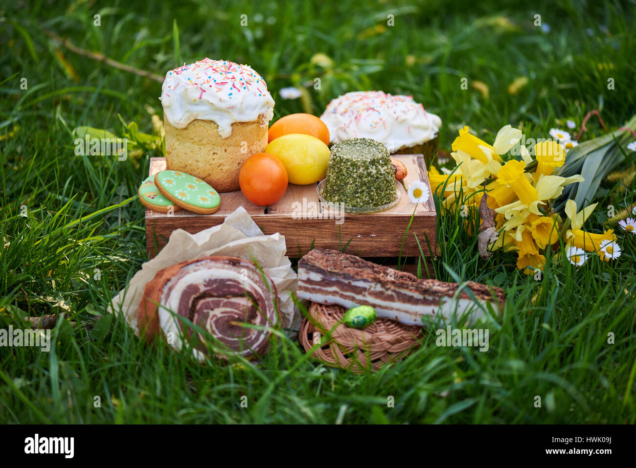 Torta di Pasqua e luminose uova colorate riuniti insieme con carne, ossequi e tulipani sul prato tra l'erba Foto Stock