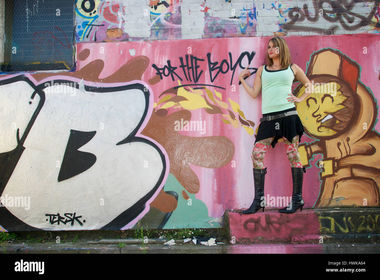 Giovane e bella donna che indossa una mini gonna e un giubbotto verde contro un coperto di graffiti wall Foto Stock