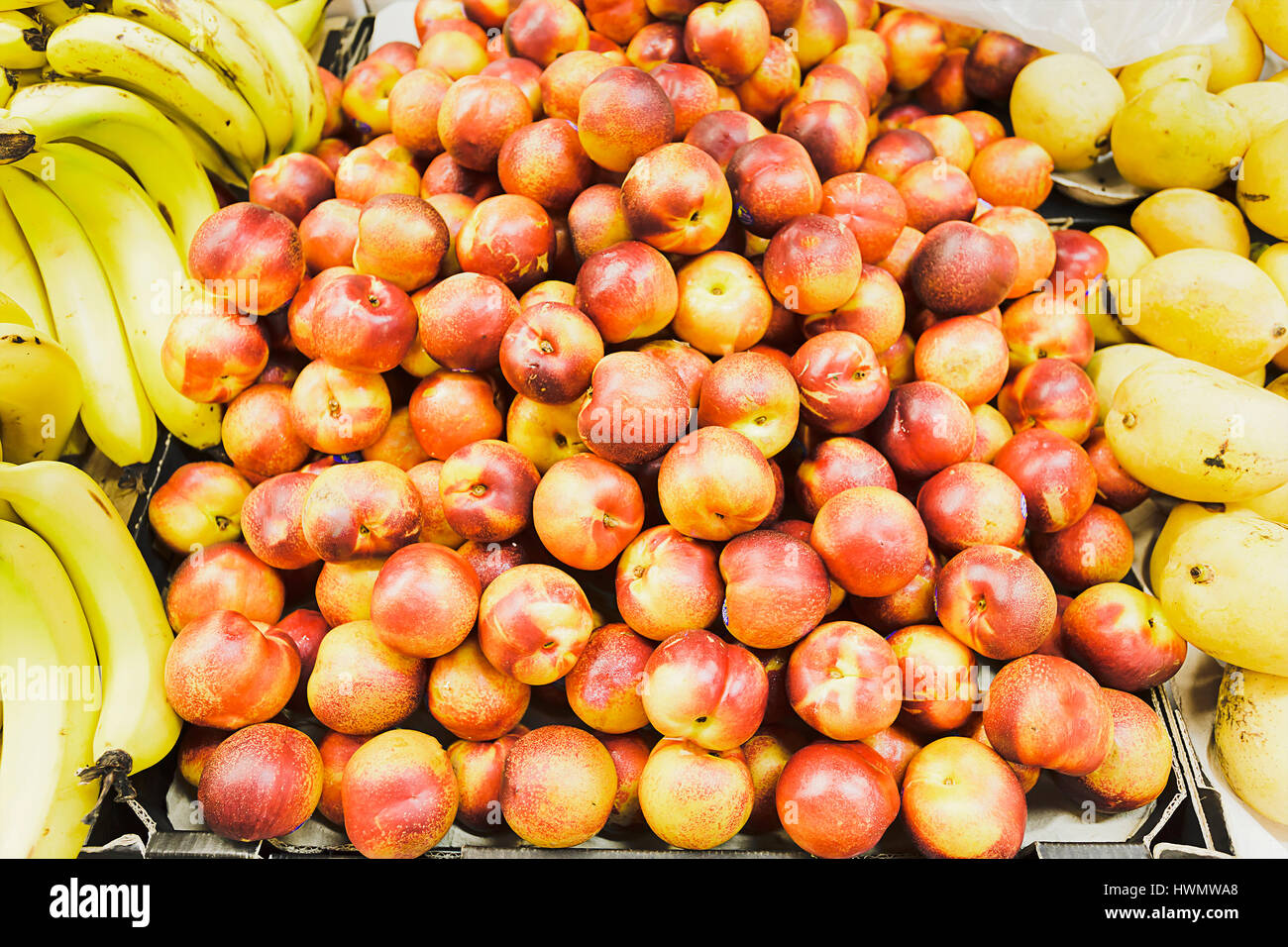 Pesche noci frutti in pietra circondato da pile di giallo banane dolci in una casella su un contatore in un mercato. Foto Stock