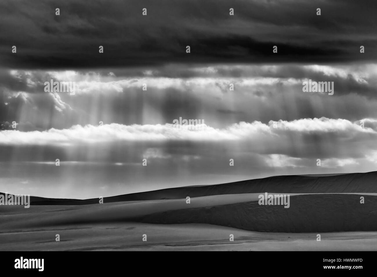 Basse nuvole temporalesche bloccando la luce solare consentendo solo i raggi luminosi a venire attraverso giù a terra - le forme delle dune di sabbia. Foto Stock