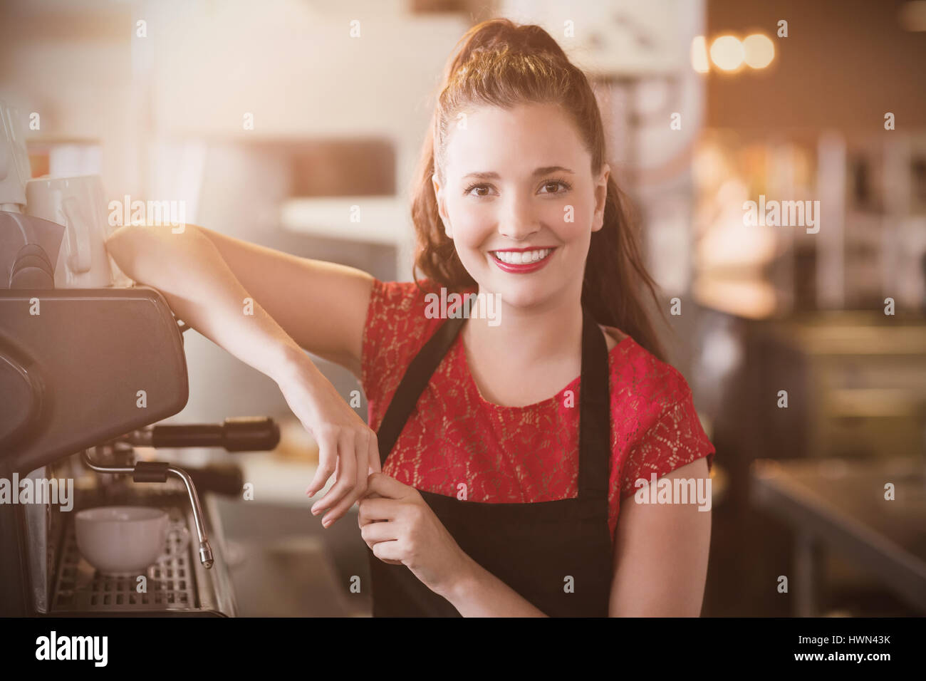 Flare contro sorridente barista appoggiata sulla macchina espresso Foto Stock