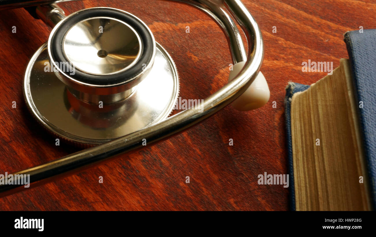 Lo stetoscopio e il libro su un sfondo di legno. Medico di fondo. Foto Stock