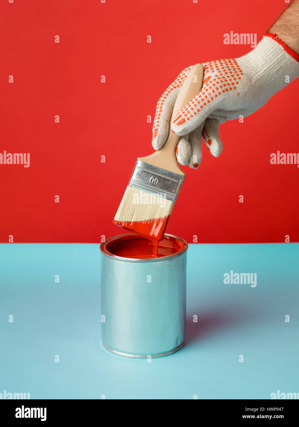 Immagine minima dipinta di fresco sfondo rosso e può con una spazzola in mano sul tavolo blu Foto Stock
