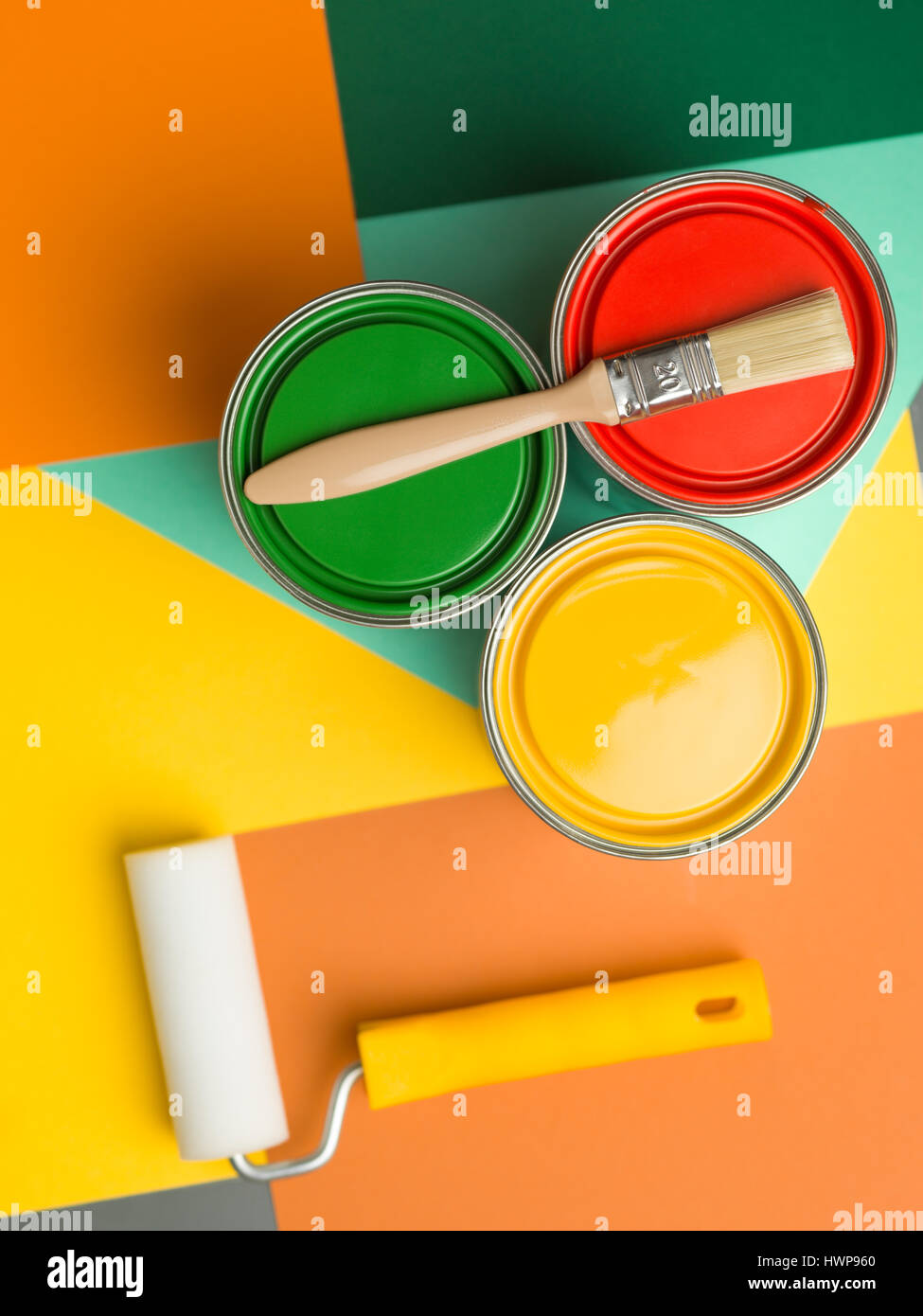 Tre lattine giallo verde e rosso e spazzola di vernice e il rotolo sul colorato sfondo geometrica Foto Stock