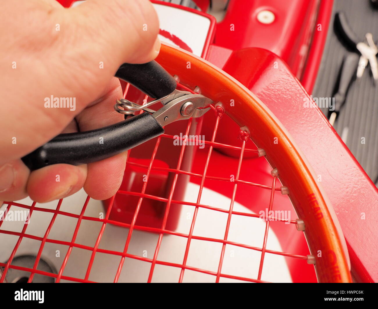 Tagliare la parte in eccesso di una croce stringhe nodo di partenza di una racchetta da tennis nel processo di tesatura su un elettronico professionale macchina di tesatura Foto Stock
