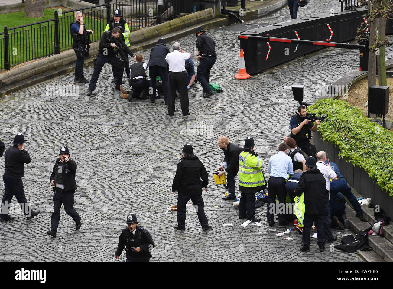 Un poliziotto punti una pistola a un uomo sul pavimento (top) mentre i servizi di emergenza frequentare lui e un funzionario di polizia (fondo) al di fuori del Palazzo di Westminster, Londra, dopo un poliziotto è stato ucciso ed il suo apparente utente malintenzionato shot da parte di funzionari in un grave incidente di sicurezza presso le Case del Parlamento. Foto Stock