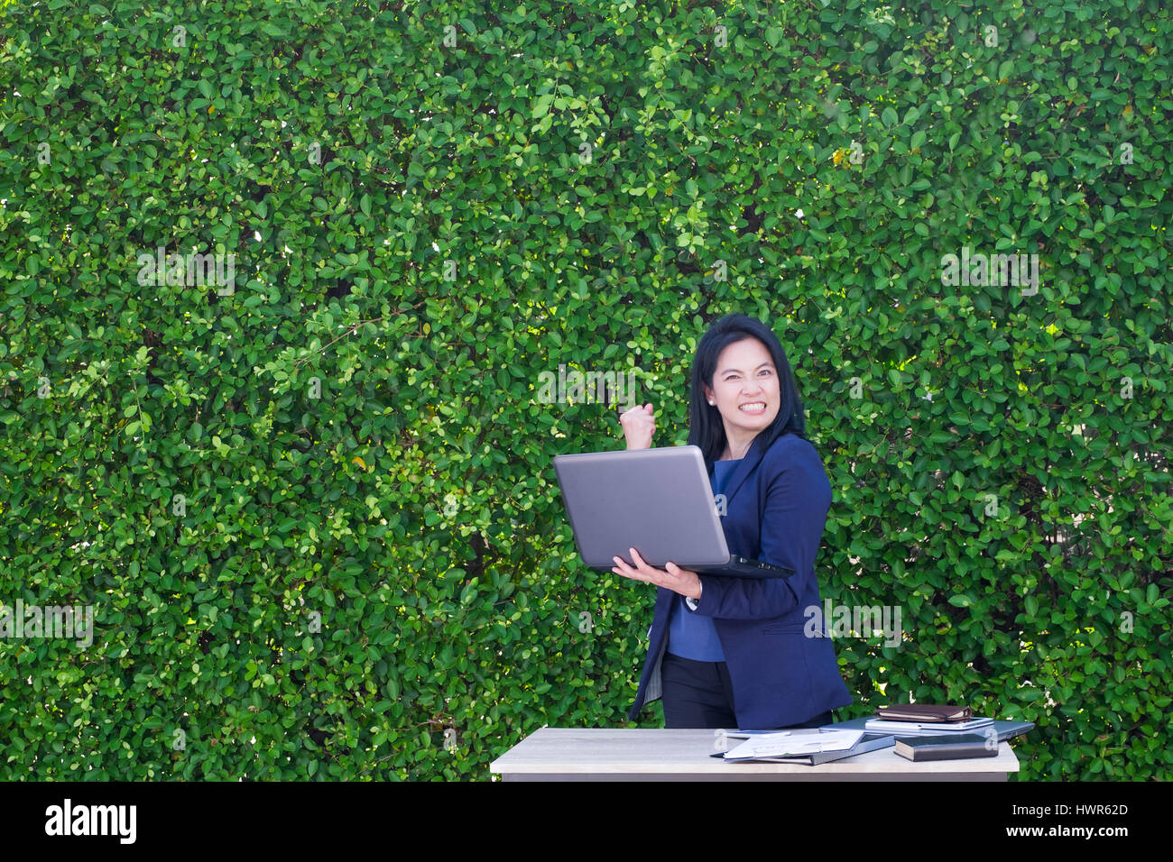 Imprenditrice braccio fino alla celebrazione di business plan successo fuori ufficio a foglia verde parete. Foto Stock