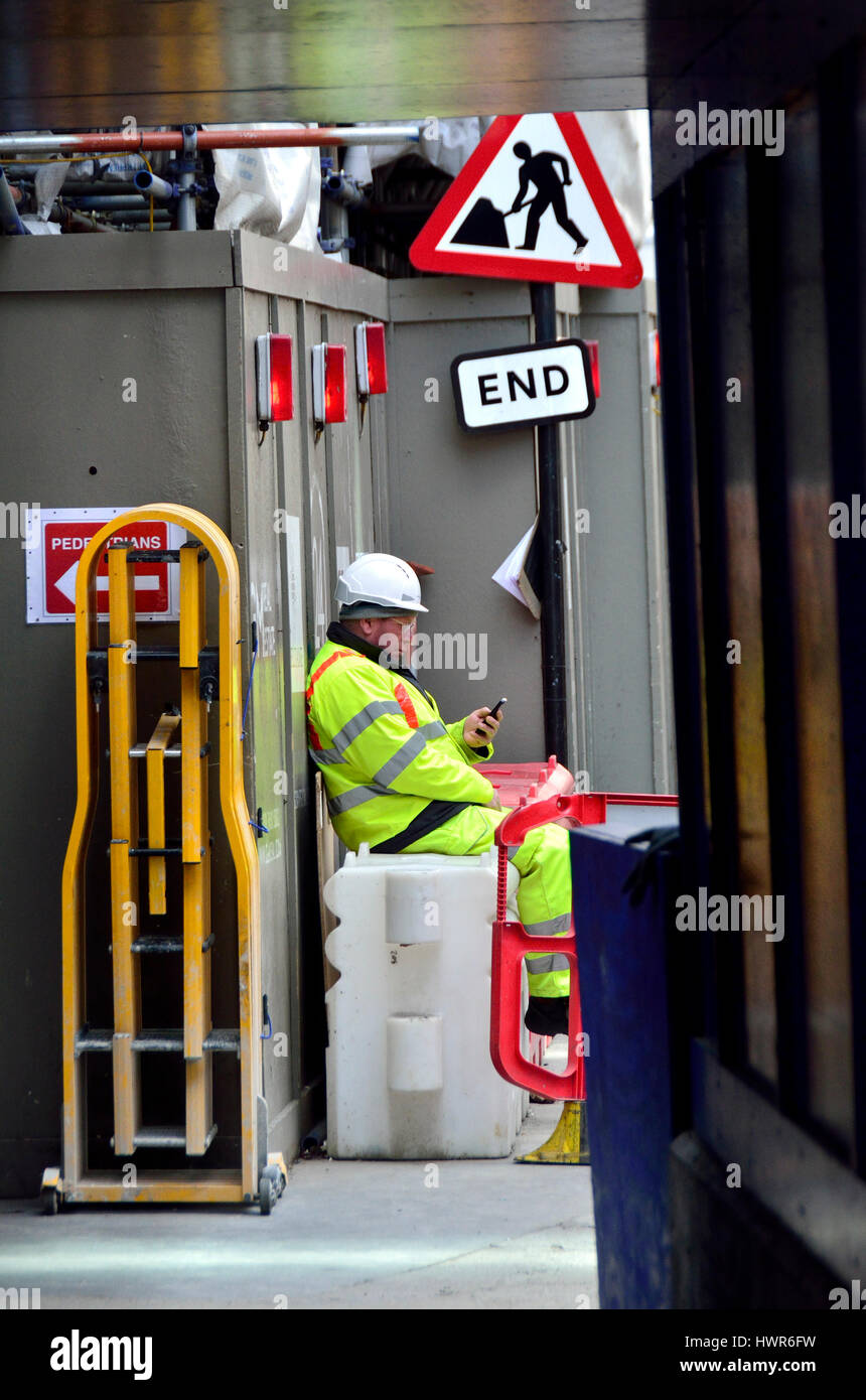 Londra, Inghilterra, Regno Unito. Costruzione di lavoratore prendendo una pausa, sul suo telefono cellulare Foto Stock