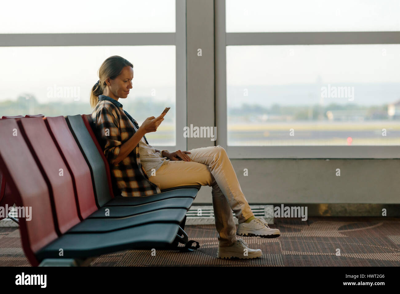 Vista laterale della donna sorridente tramite cellulare in aeroporto area di partenza Foto Stock