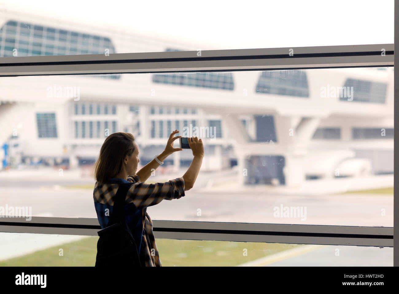 Donna fotografare attraverso la finestra mentre in piedi in aeroporto area di partenza Foto Stock