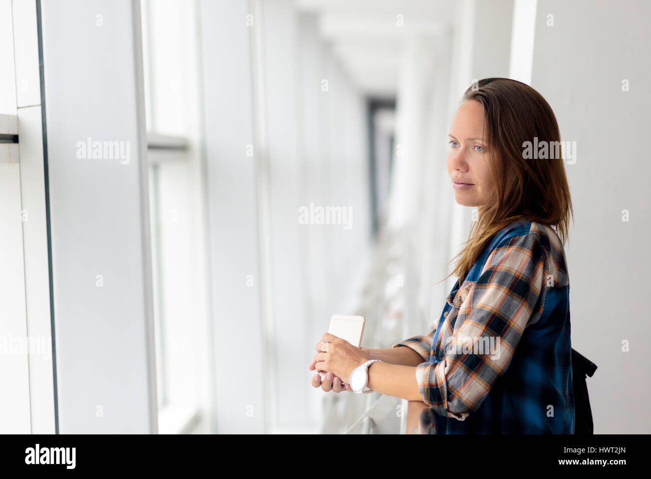 Premurosa donna che guarda attraverso la finestra mentre in piedi dalla ringhiera in aeroporto Foto Stock
