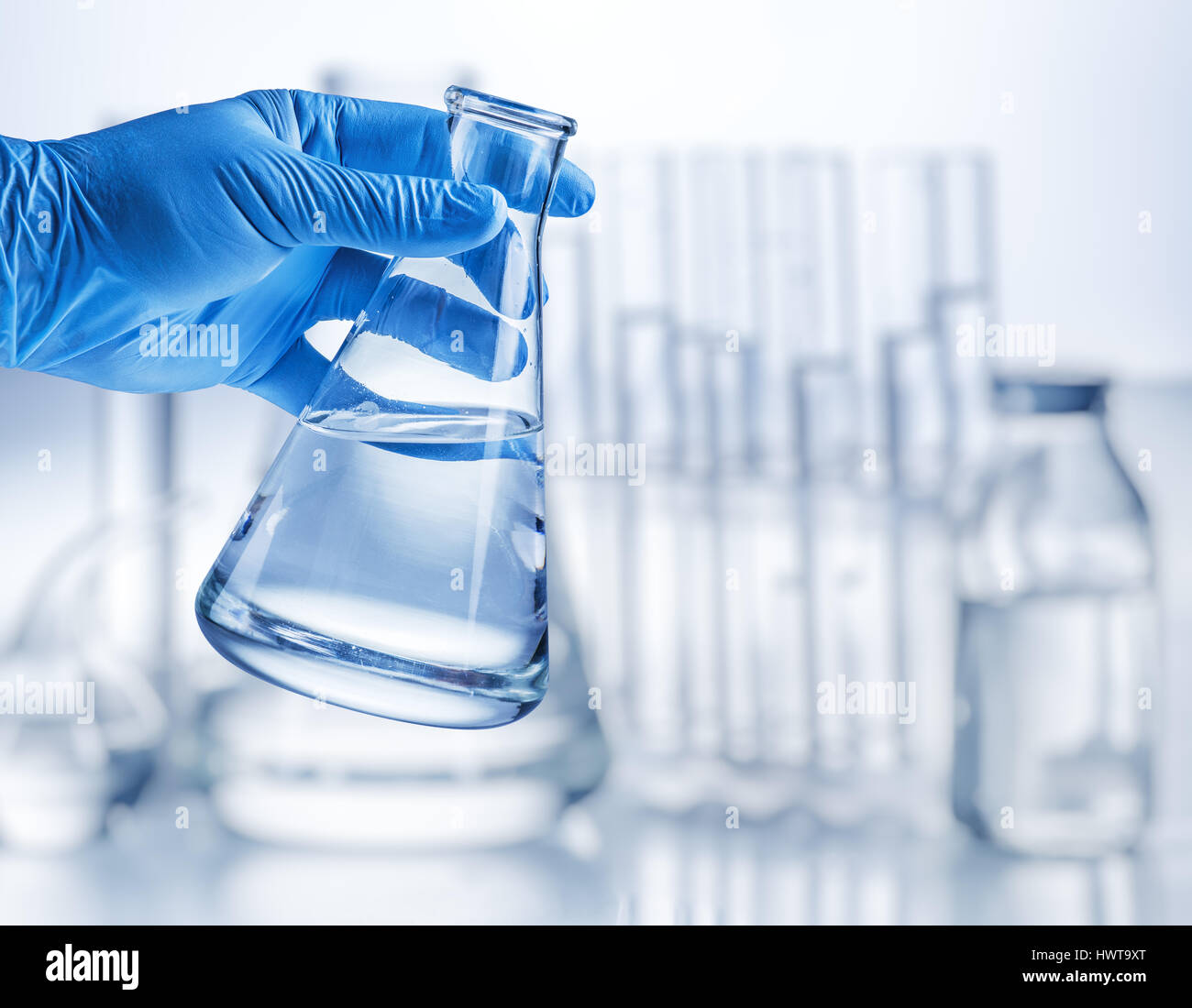 Bicchiere da laboratorio in analyst la mano nel guanto di plastica. Foto Stock